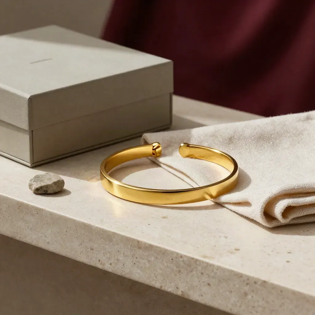 Bracciale in oro satinato con lino, scatolina neutra e pietra su fondo chiaro.